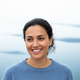 Close-up portrait of a happy person in their 30s, smiling gently, with a soft, blurred background of white and blue.